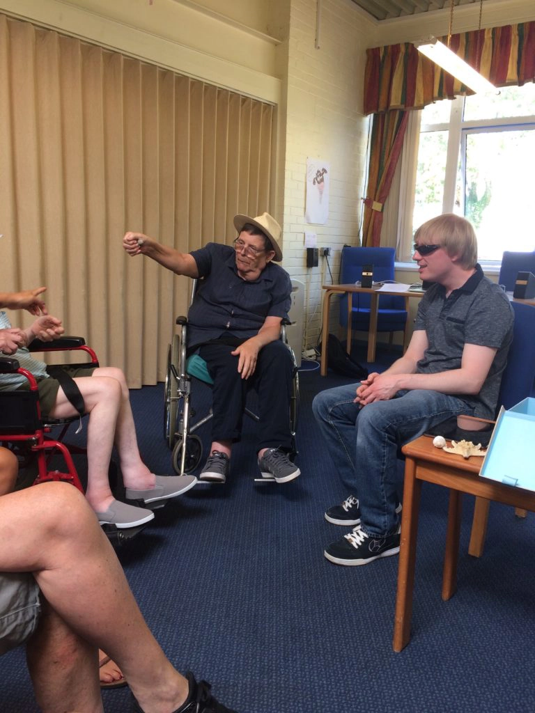 Included is a picture of participants sitting on chairs in a circle, sharing objects from the seaside.