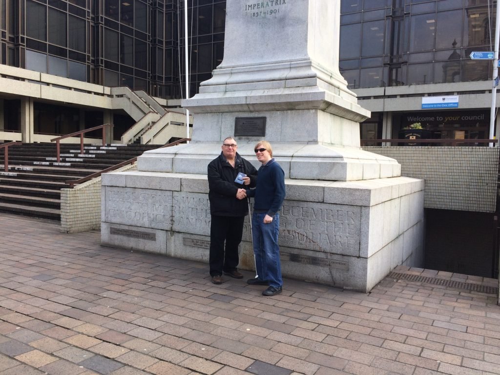 Included is a picture of Dave Taylor from Losing My Sight UK, and David Shervill from Global Music Visions C.I.C. shaking hands, whilst standing in front of the Victoria Monument in Guildhall Square Portsmouth. Dave Taylor is holding the memory stick in his left hand.