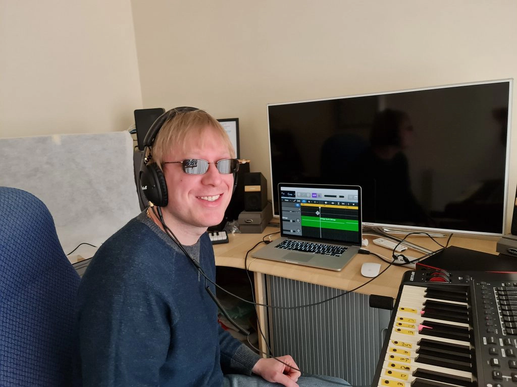 Included is a picture of David Shervill (Founder) sitting at a desk wearing headphones connected to the sound card on his right, with the laptop open directly in front of him, with a music project open on it. Speakers are each side of the laptop. There is a MIDI keyboard further round on his right.