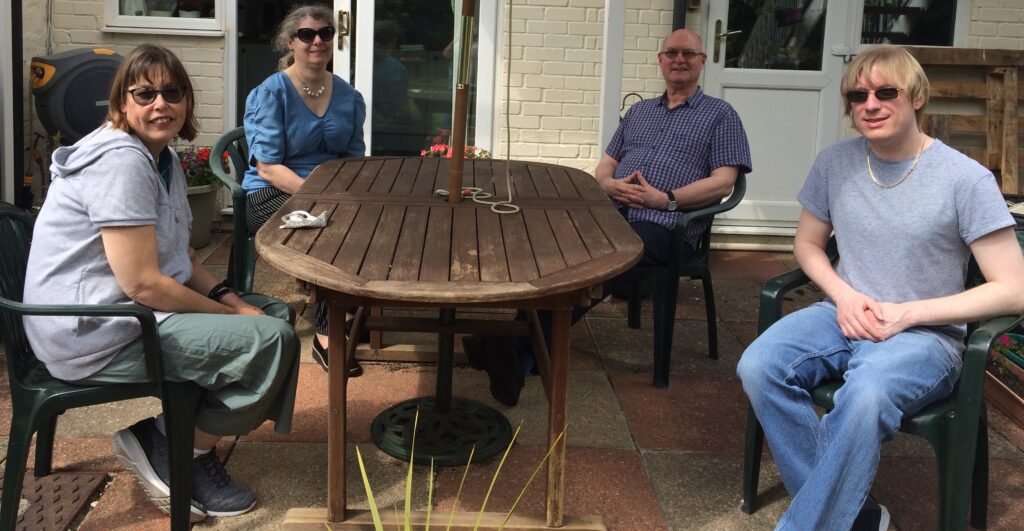 Included is a photo of four people, including David sitting around a garden table outside, all facing the camera.
