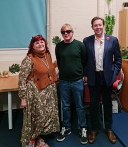 Standing from left to right are Caz Gilmore Teaching Assistant, David Shervill, founder of Global Music Visions C.I.C. and Cllr Chris Attwell. All are facing the camera with a smile, with class room table and cupboards behind them.