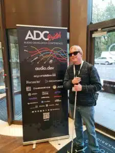 David Shervill standing to one side of the ADC 25 pull up banner at the entrance of the event.